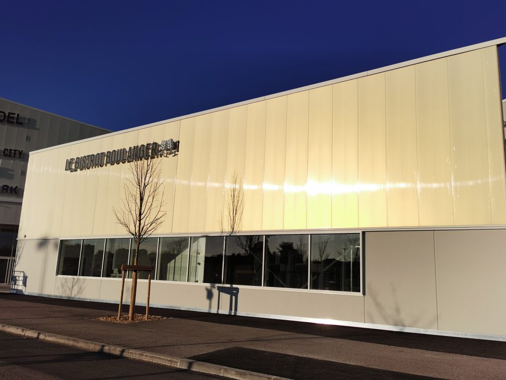 Bâtiment vu d'une rue avec un bardage en plaques de polycarbonate alvéolaire. Le système emboîtable arcoPlus® 549 est résistant aux UV.