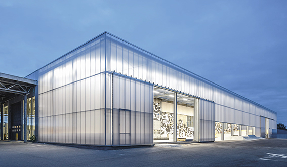 Bâtiment vu d'une rue avec un bardage en plaques de polycarbonate alvéolaire. Le système emboîtable arcoPlus® 549 est résistant aux UV.