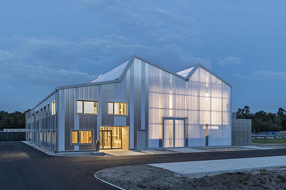 Bâtiment vu d'une rue avec un bardage en plaques de polycarbonate alvéolaire. Le système emboîtable arcoPlus® 549 est résistant aux UV.