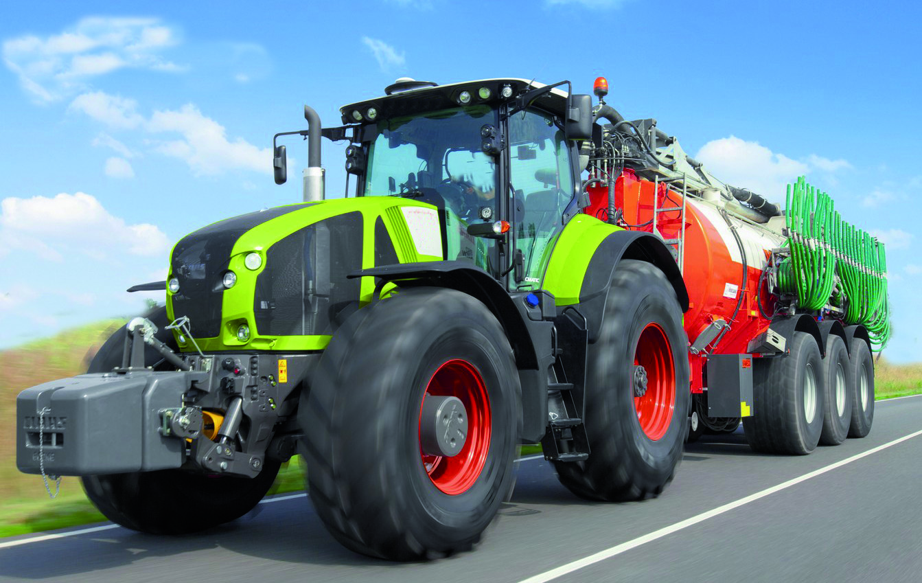 Un tracteur de couleur verte et rouge traverse une route. Ce dernier illustre les applications possibles du polycarbonate compact pour l'aménagement de véhicules